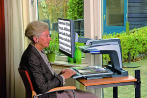Eine ältere Dame sitzt vor einem Bildschirmlesegerät