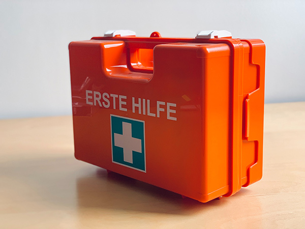 Ein orangefarbener Erste-Hilfe-Koffer mit einem weißen Kreuz auf blauem Hintergrund