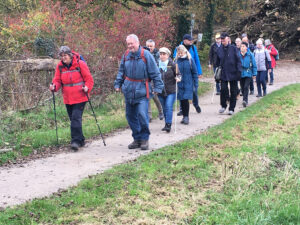 Eine Gruppe von Menschen wandert auf einem Feldweg durch ein Waldgebiet, einige benutzen Wanderstöcke andere Blindenstöcke.