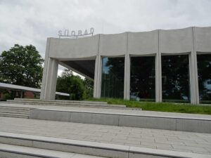 Das Bild zeigt einen Teil der Gebäudefassade des Südbades. Fünf weiße Betonpfeiler im Abstand von 3 Metern tragen einen senkrecht wellenförmigen Dachsturz. Zwischen den Pfeilern sind getönte Glasflächen. Auf dem Flachdach ist der Name „Südbad“ angebracht.